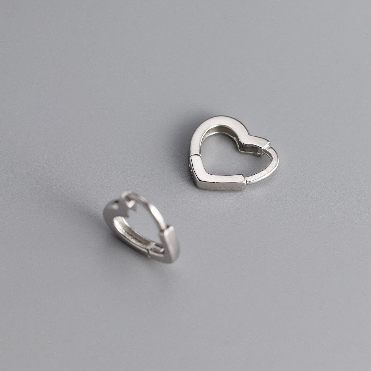 Two silver heart-shaped hoop earrings on a gray background