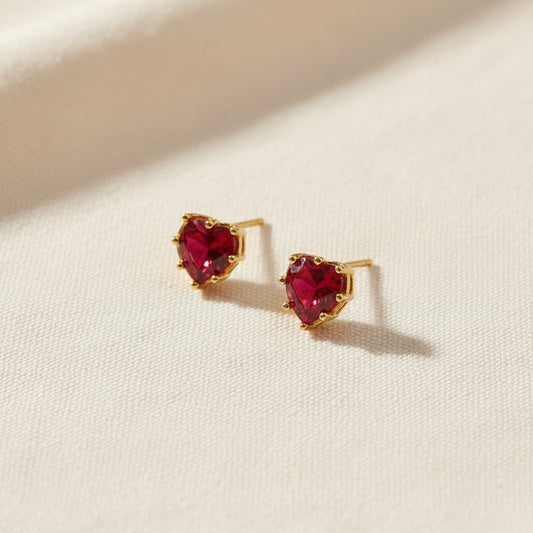 Heart-shaped red gemstone earrings with gold accents on a white background