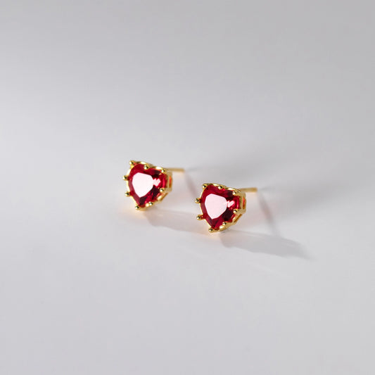 Heart-shaped red gemstone earrings with gold accents on a light gray background