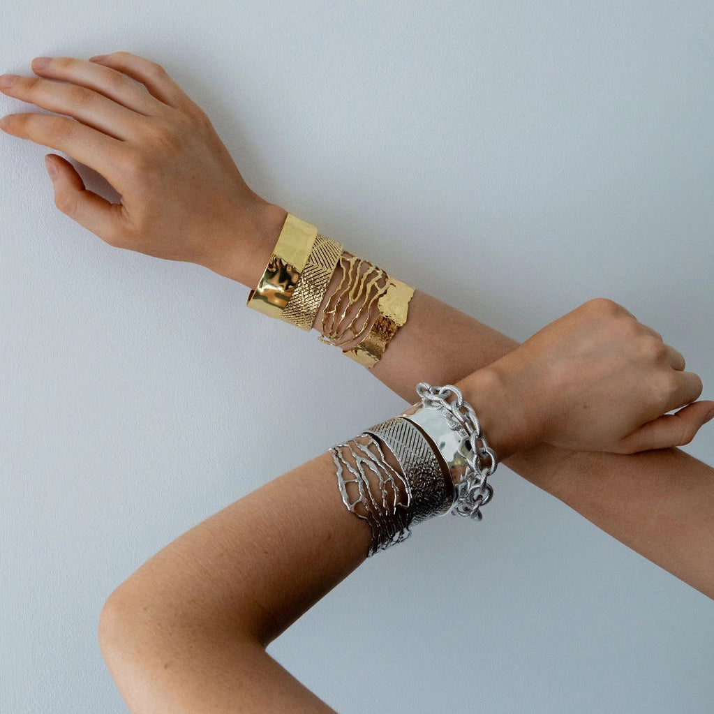 Two arms wearing gold and silver bracelets on a light gray background