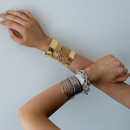 Two arms wearing gold and silver bracelets on a light gray background