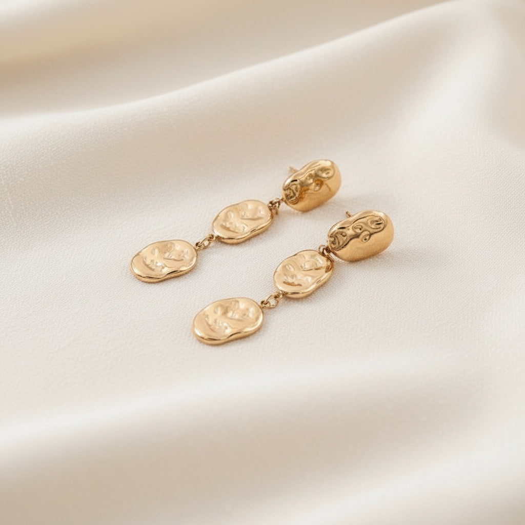 Gold earrings on a warm white background
