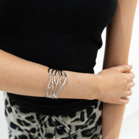 Person wearing a black top and leopard print pants with silver bracelets on a white background