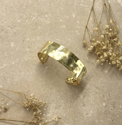 Gold bracelet on a textured surface with dried flowers