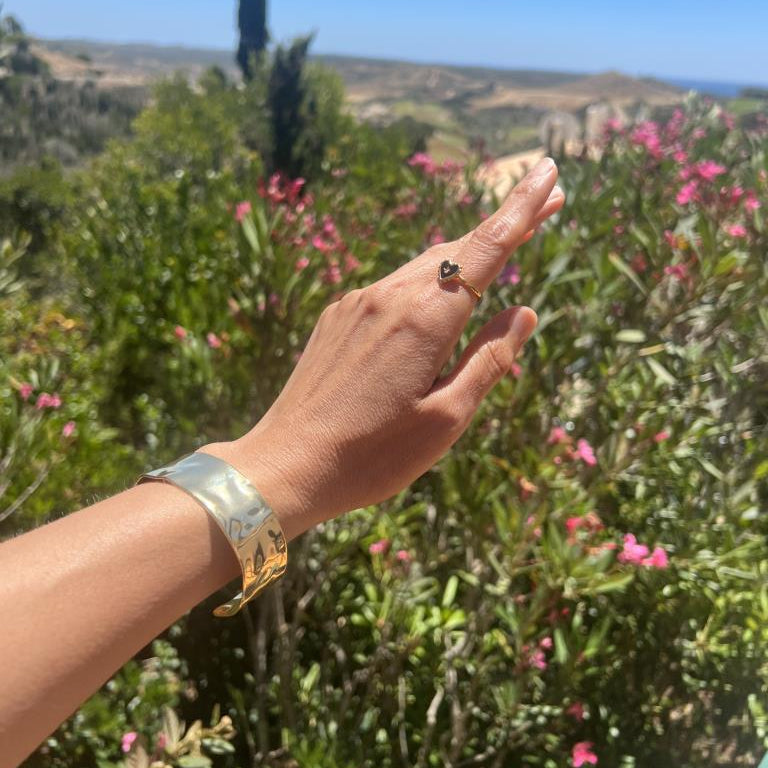 Hand pointing towards a scenic landscape with greenery and flowers. Wearing a gold bangle
