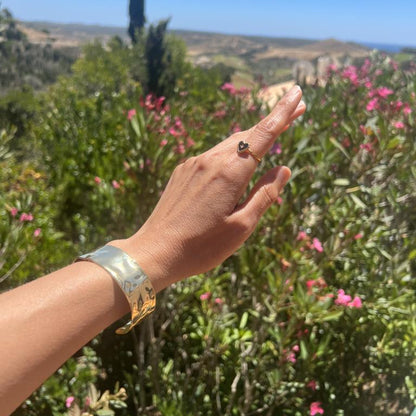 Hand pointing towards a scenic landscape with greenery and flowers. Wearing a gold bangle