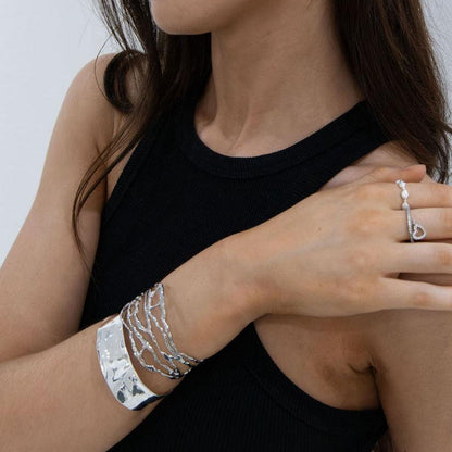 Close-up of a person wearing silver bracelets and a ring on a plain background