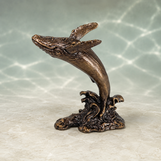 Bronze-finished sculpture of a whale leaping from the sea, mounted on a wave-like base, displayed against a light gray background with a soft water ripple pattern.