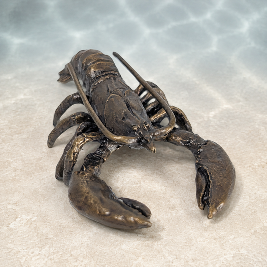 A realistic lobster sculpture with a metallic bronze finish, displayed on a light beige textured surface with a water ripple effect in the background.