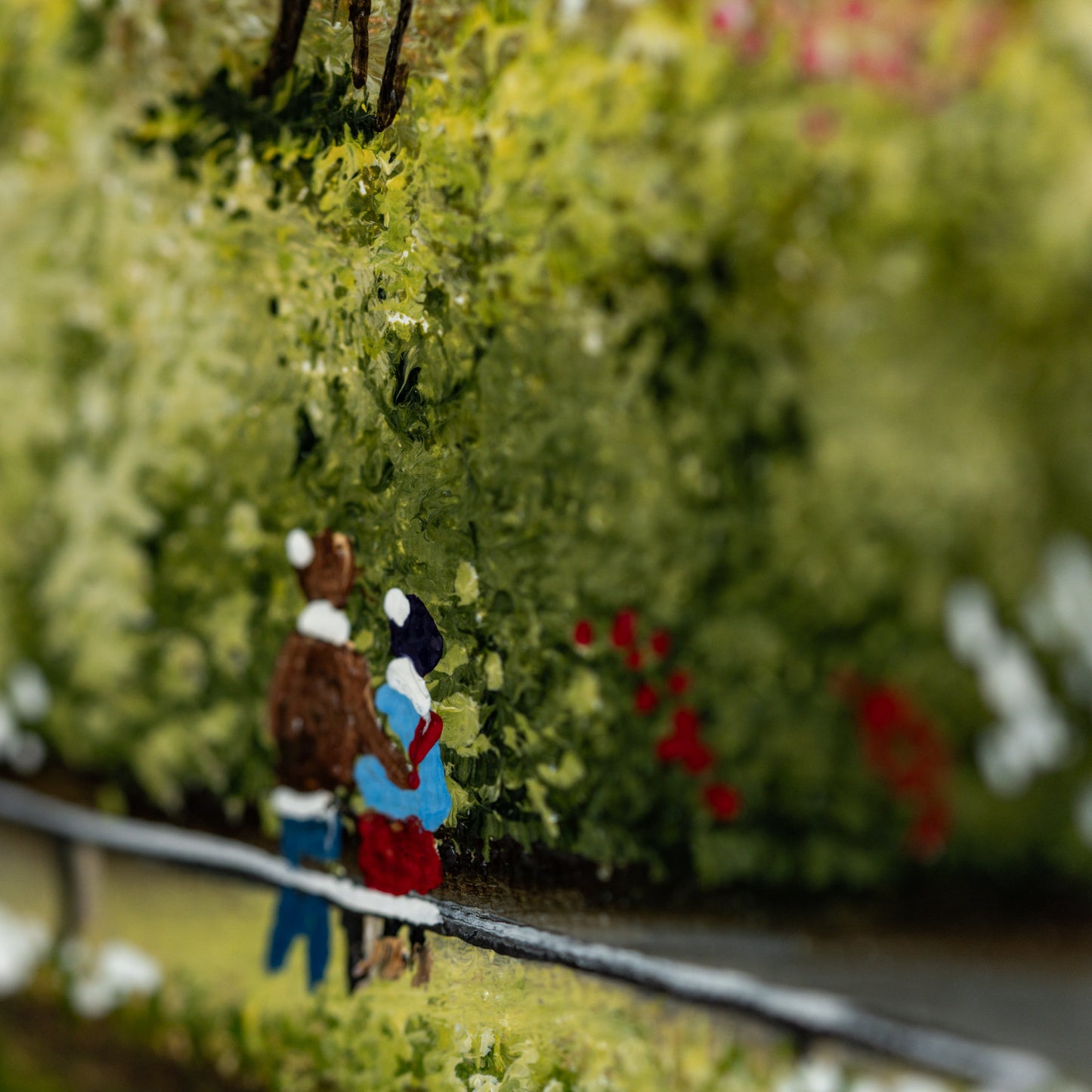 Two figurines standing close together in a forest setting with green trees and red flowers.