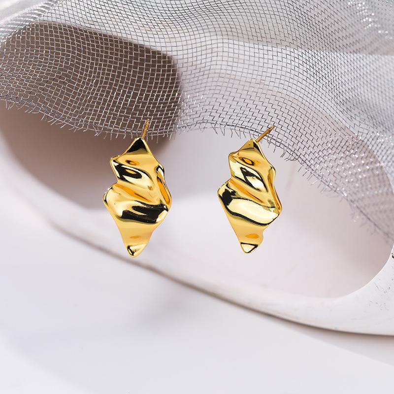 Gold earrings on a white surface with a light gray fabric background