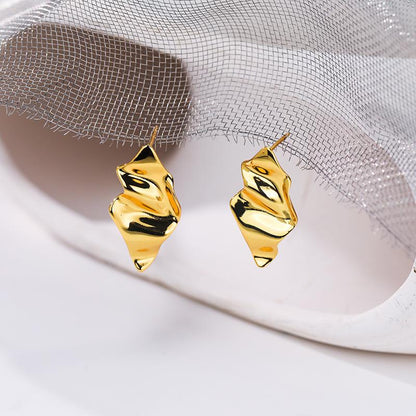 Gold earrings on a white surface with a light gray fabric background