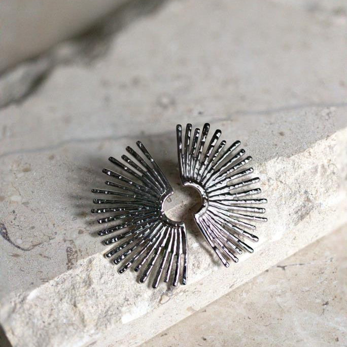 Silver sunburst earring on a stone surface with greenery in the background
