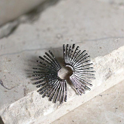 Silver sunburst earring on a stone surface with greenery in the background