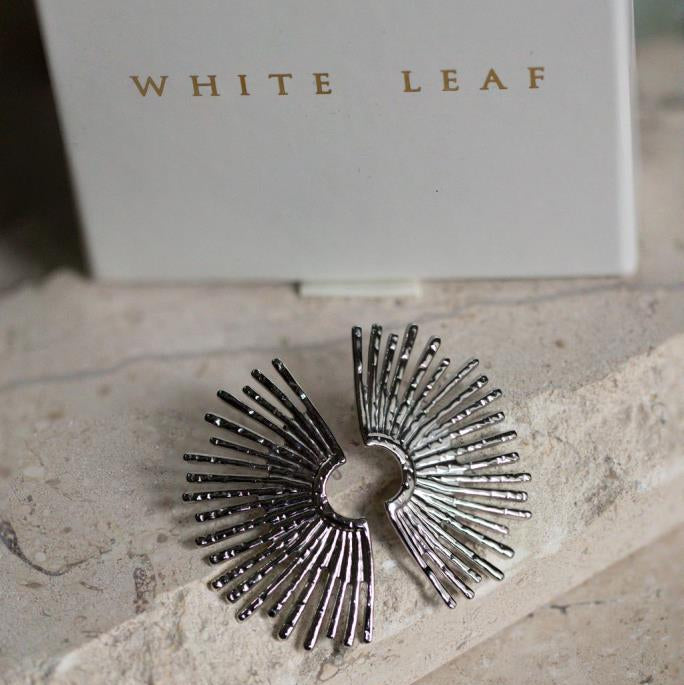 Silver sunburst ring on a stone surface with 'White Leaf' branding in the background.