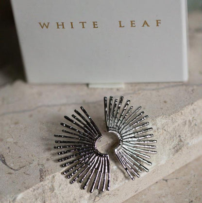 Silver sunburst ring on a stone surface with 'White Leaf' branding in the background.