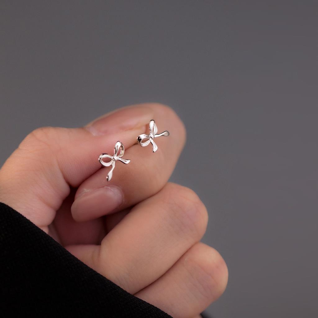 Silver bow-shaped earrings held between fingers against a dark background