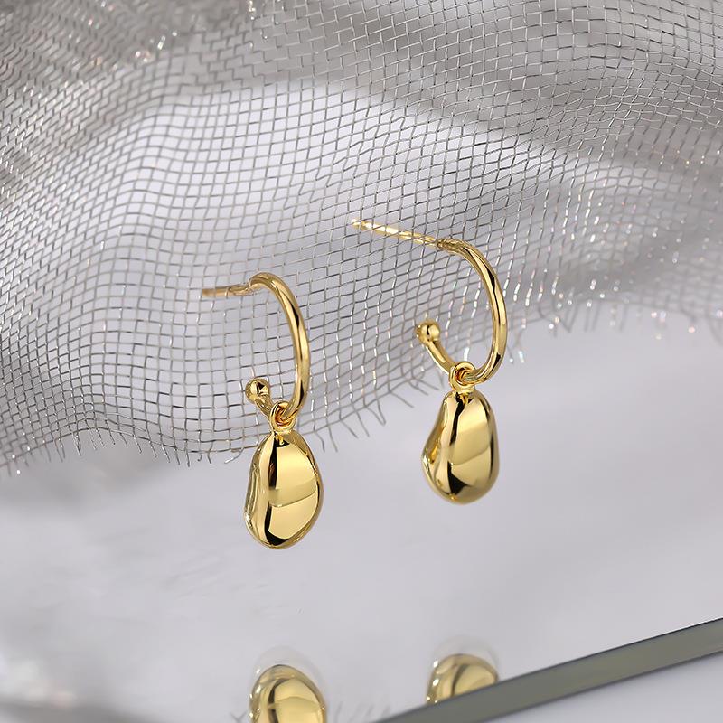 Gold teardrop earrings on a textured silver background