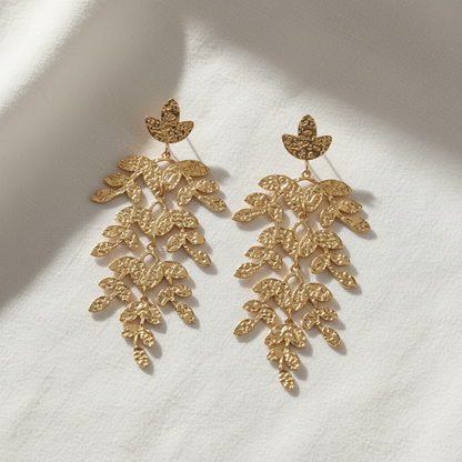 A pair of gold-toned dangle earrings with a leaf design, shown against a plain white background.