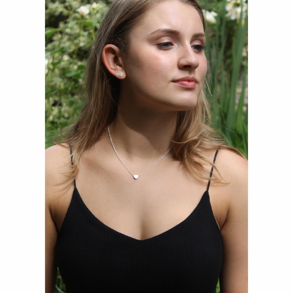 Woman wearing a black top and silver necklace with a heart pendant outdoors.