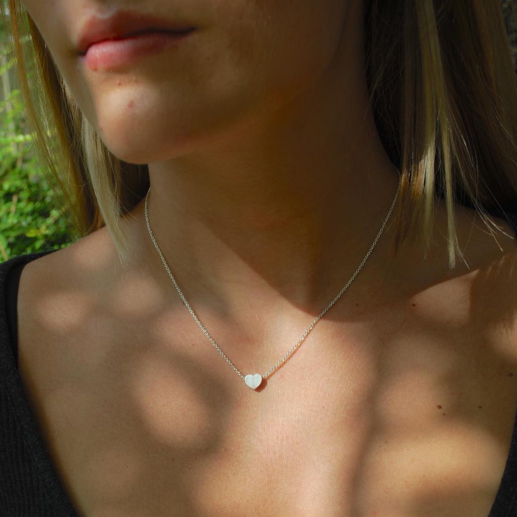 Close-up of a person wearing a delicate necklace with a heart pendant outdoors.