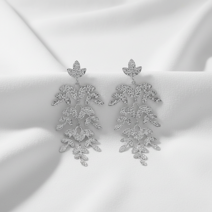 A pair of silver-toned dangle earrings with a cascading, leaf-like design set with clear rhinestones, shown against a plain white background.