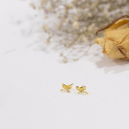 Gold butterfly earrings on a white surface with dried flowers in the background
