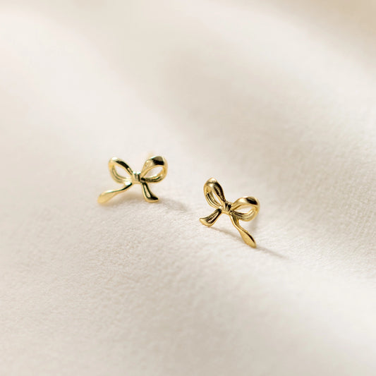 Gold bow-shaped earrings on a light beige background