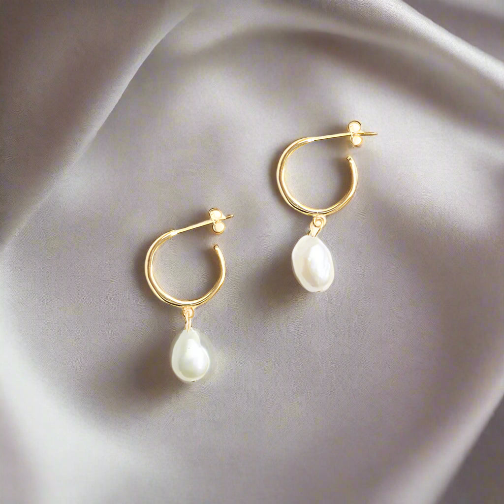 Gold hoop earrings with pearl drops on a white background
