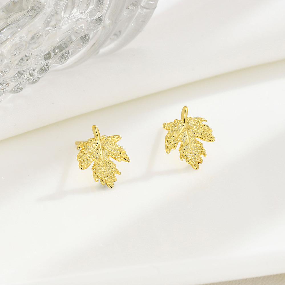 Gold leaf-shaped earrings on a white surface