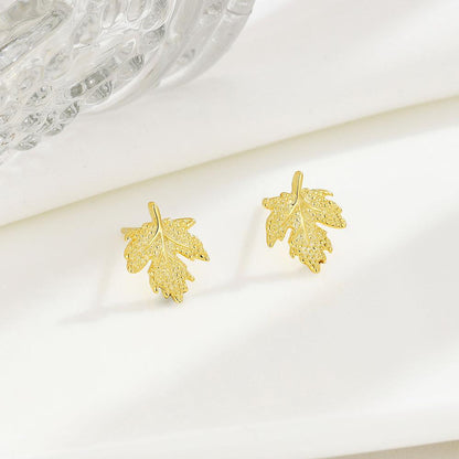 Gold leaf-shaped earrings on a white surface